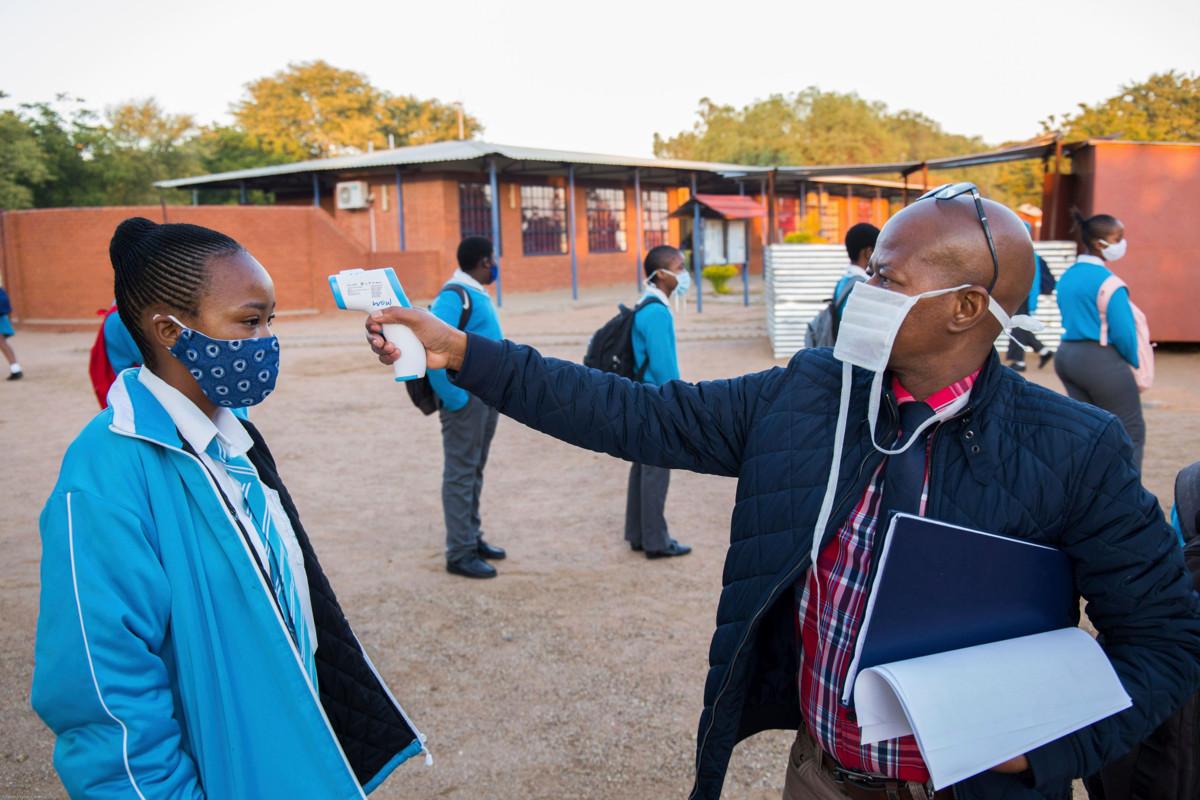 Opettaja tarkistaa oppilaan ruumiinlämmön ennen kuin päästää hänet luokkaan. Kuva on Botswanan pääkaupungista Gaboronesta.