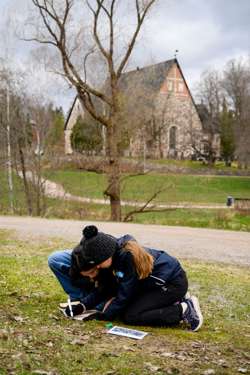 Olivia Houttu ja Minni Ruokolahti toisen rastin tehtävän kimpussa. Taustalla näkyy 1400-luvulla rakennettu Espoon tuomiokirkko.