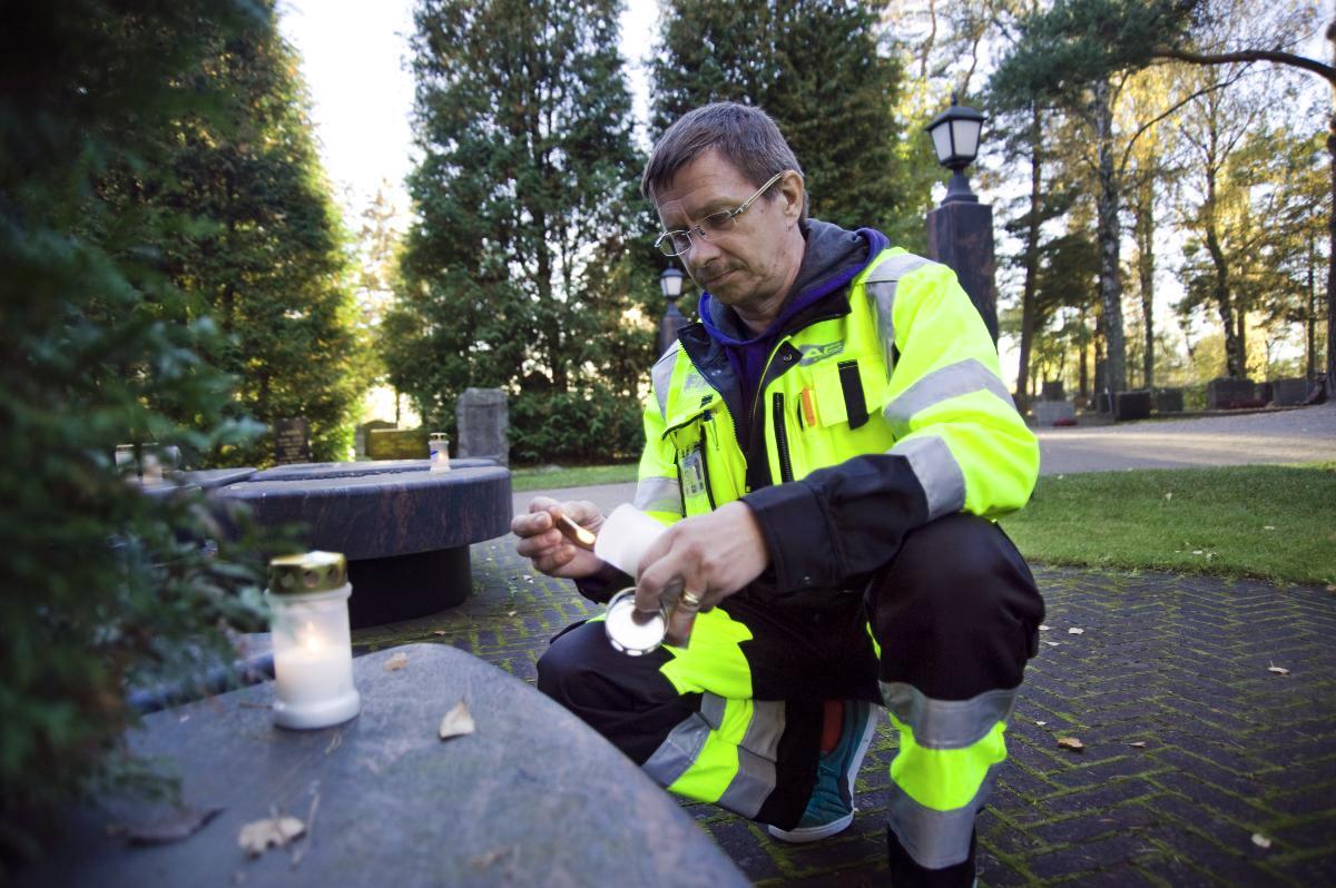 Erkki Pulkkinen sytyttää kynttilän vuosi sitten kuolleen ystävänsä haudalle. Kuva: Marianna Siitonen