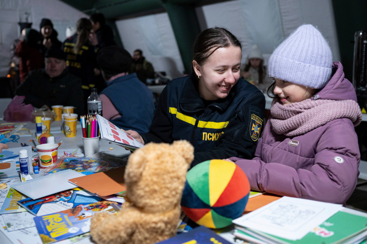 Ukrainan valtion pelastuspalvelun psykologi keskustelee lapsen kanssa liikkuvassa lämmityspisteessä Kiovan Troieshchynan asuinalueella. Venäjän iskut energiainfrastruktuuriin ovat katkaisseet alueelta sähkön ja lämmityksen. Kuva on otettu 21. tammikuuta 2026. Kuva: Danylo Antoniuk/Lehtikuva/Sipa Press.