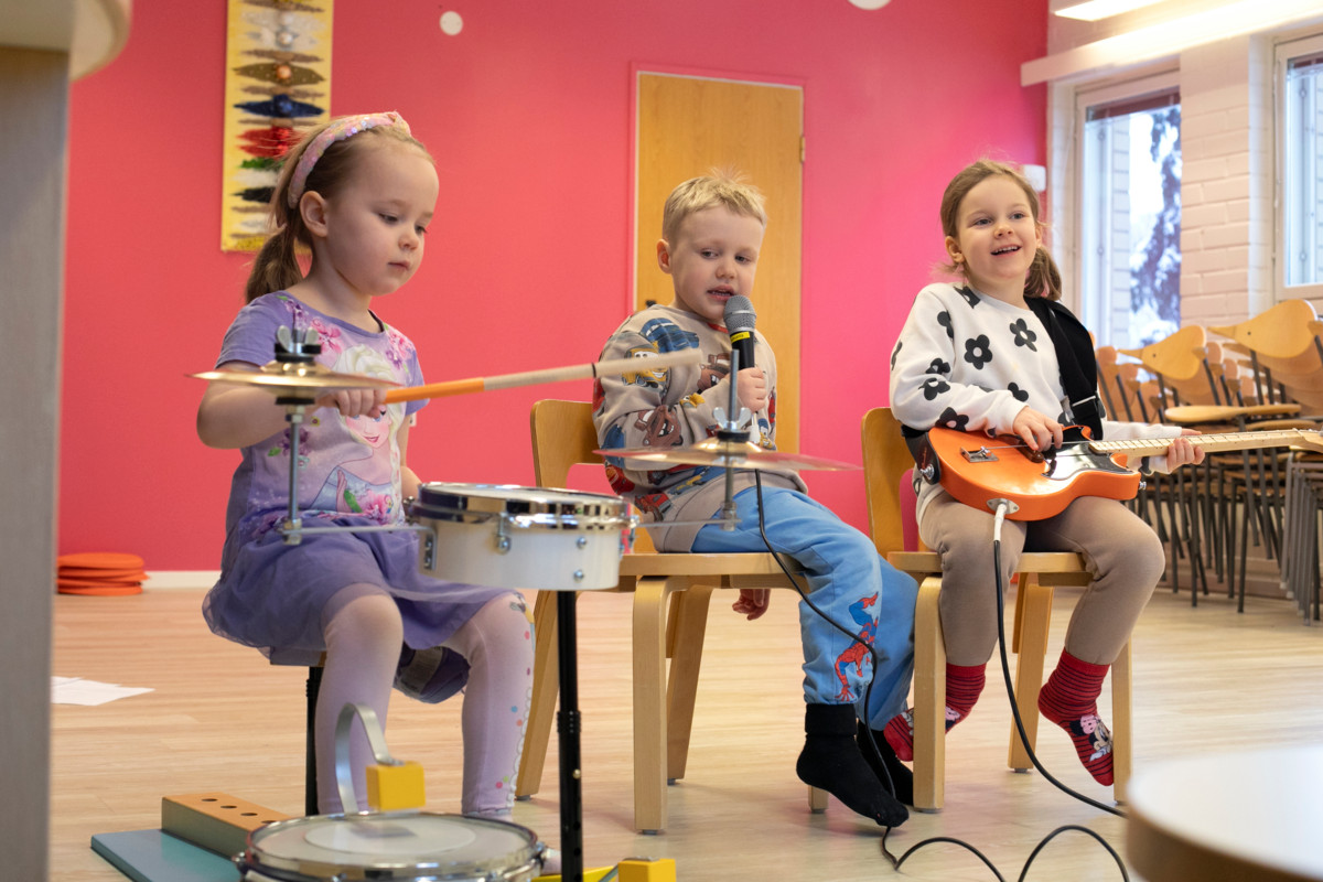 Esme Haikarinen soitti rumpuja, Roope Europaeus lauloi ja Eleonora Serolimos-Hakamäki soitti kitaraa vekarabändin harjoituksissa.