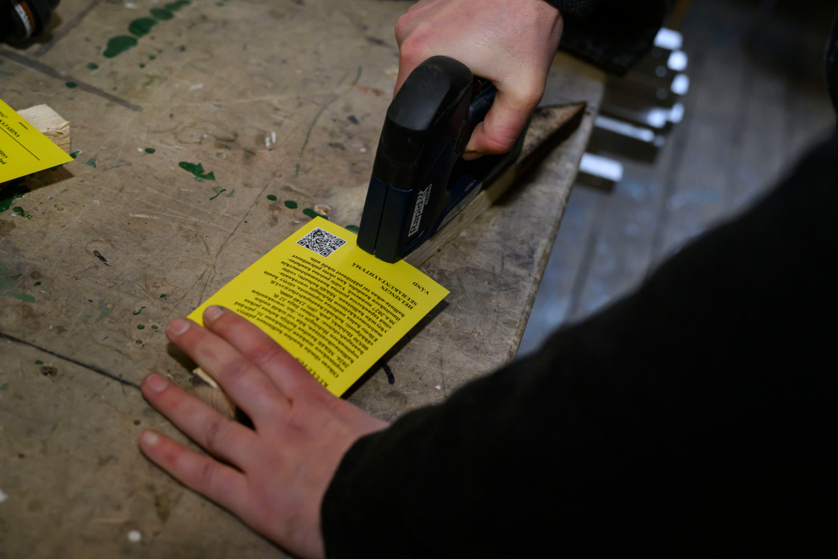 Sebastian Tjäder nitoo kuulutuskylttiä sahaamaansa keppiin puuverstaalla. 