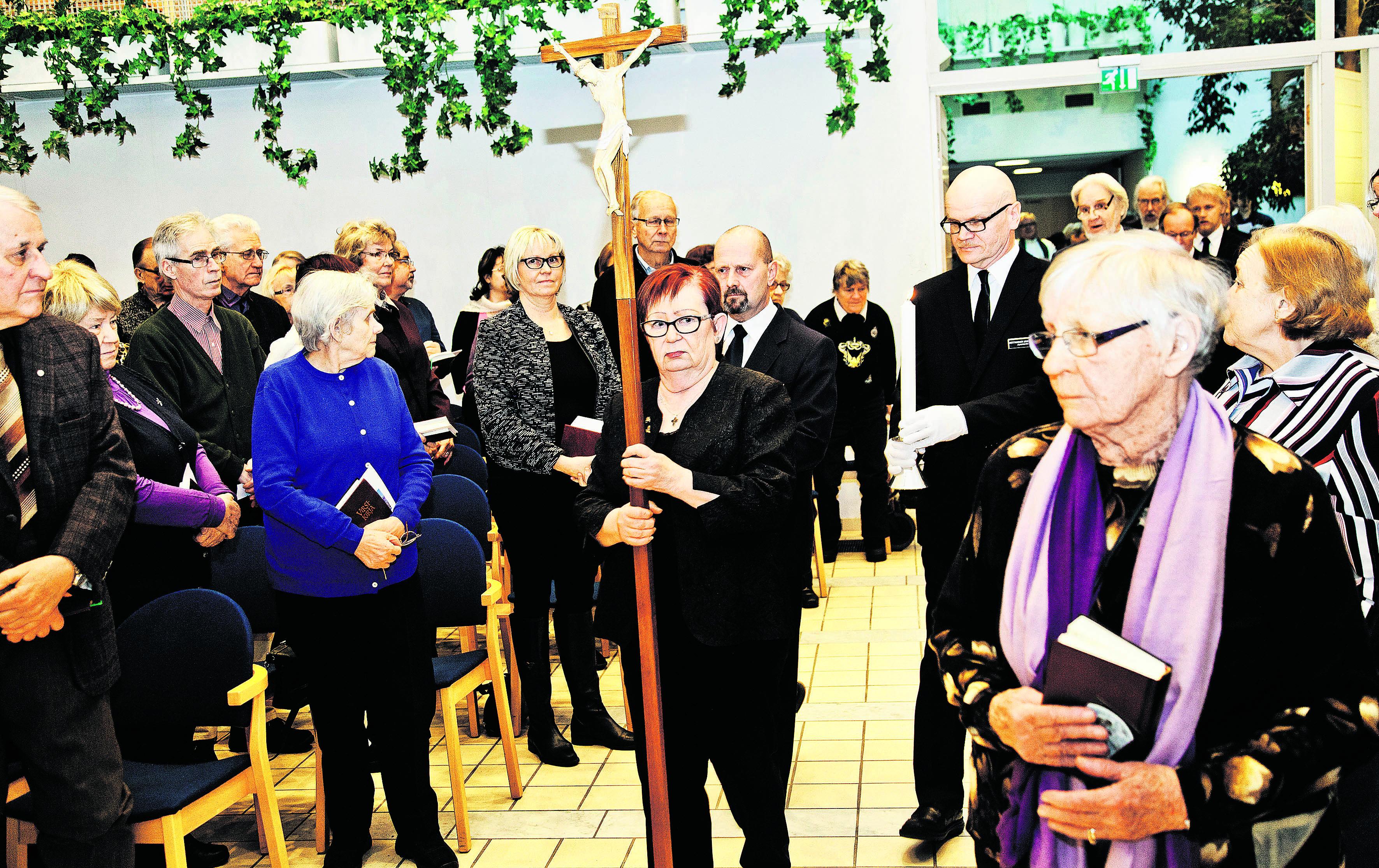 Messu alkaa. Sinikka Backman johdottaa ristikulkueen kirkkosalin. Paikalle on saapunut runsaasti erityisesti keski-ikäisiä ja sitä vanhempia kirkkovieraita.