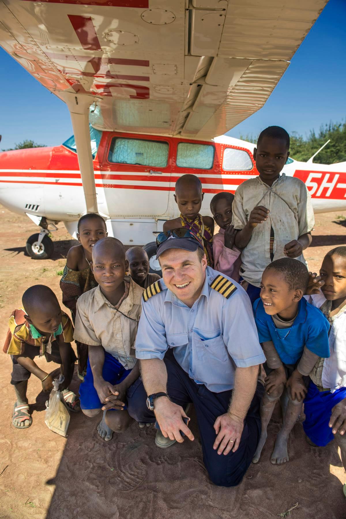 Lähetyslentäjä Jarkko Korhonen Dabian kiitoradalla tansanialaislasten kanssa. Kuva on MAF Tansanian terveydenhuoltoon keskittyvältä Kilimatiden lento-safarilta.