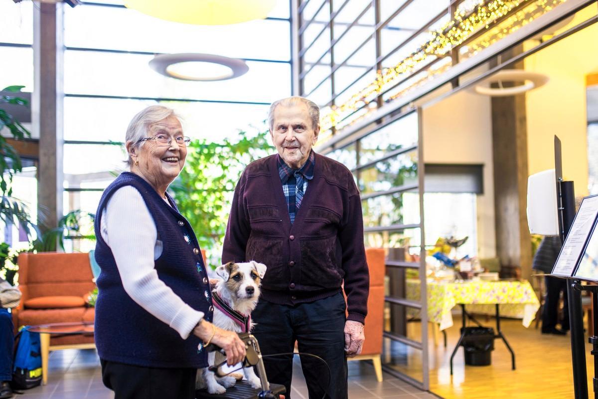 Ritva Kauramäki ja Veikko Peltola ovat tyytyväisiä elämäänsä Foibekartanossa. Talon koira on päässyt rollaattorin kyytiin.