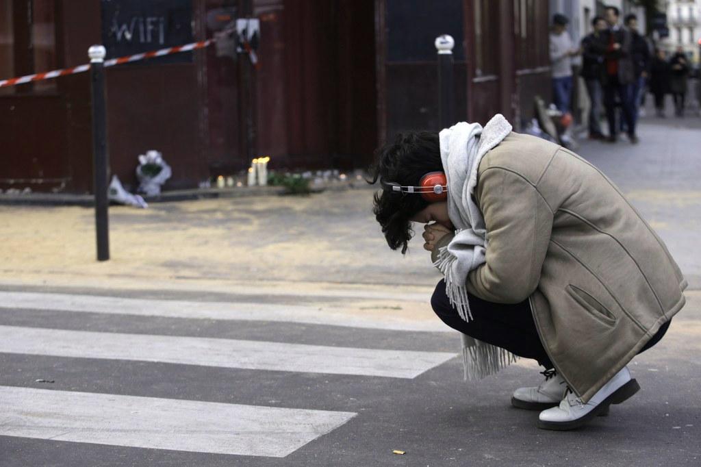 Suru on vallannut kadut. Nuori nainen polvistuu Pariisissa, lähellä iskun kohteeksi joutunutta Le Petit Cambodge -ravintolaa. Kuva: Lehtikuva
