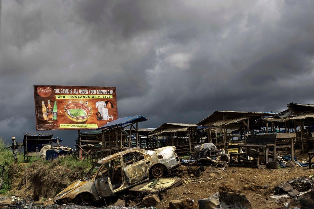 Separatistien tuhoamaksi väitetty auto seisoo autiolla markkinapaikalla Kamerunin englanninkielisen alueen Buean kaupungissa. Kaupungissa on 300 000 asukasta. Lokakuussa 2018 otetussa kuvassa vasemmalla on armeijan sotilas. Kuva: Marco Longari / Lehtikuva – AFP
