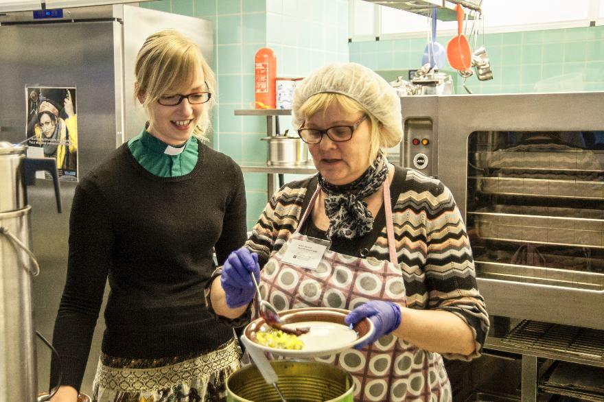 Diakonissa Sanna Tuusa seuraa, kuinka vapaaehtoistyöntekijä Erja Rautiainen jakaa ruokaa kirkon ruokailussa Tikkurilan seurakunnan nuorisotilassa. Kuva: Antero Harju