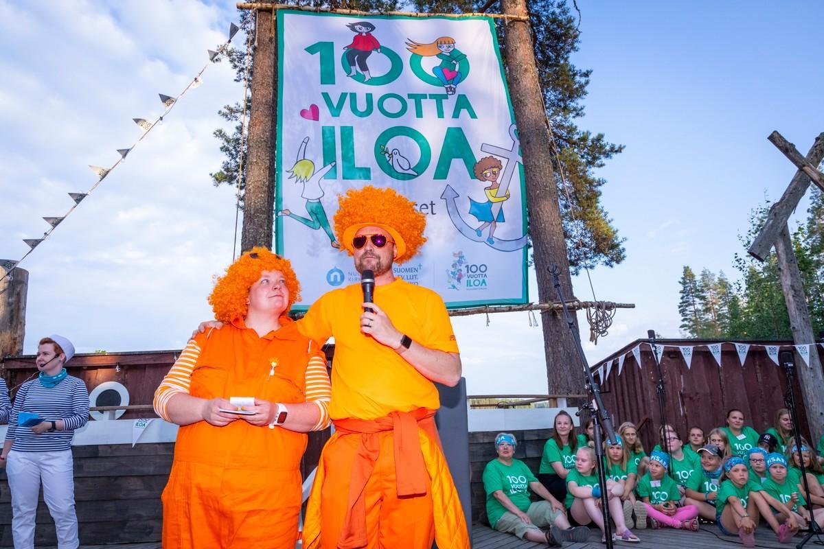 Pääkaupunkiseudun lasten ja nuorten alaleirin johtajat Stella Björkholm ja Pauli Syrjö esittäytyvät koko leirille avajaisiltanuotiolla. He ovat pukeutuneet Purolan väriin, oranssiin.