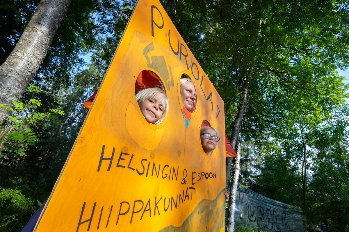 Helsinkiläiset Evelia, Pinja ja Aada Koivisto kurkistavat Purolan alaleirin leiriportista.