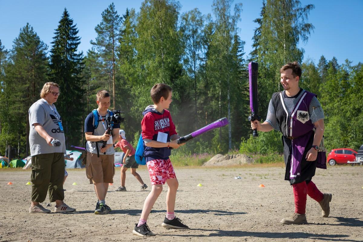 Pisara-leirin medialeiriläiset kiertävät ympäri leiriä kuvaamassa sen tapahtumia. Kuvassa Johannes kokeilee pehmomiekkailua Johnin avustuksella. Taustalla Joonas kuvaa ja medialeiriläisten ohjaaja, Nuori kirkon Tuukka Joru, valvoo tilannetta.