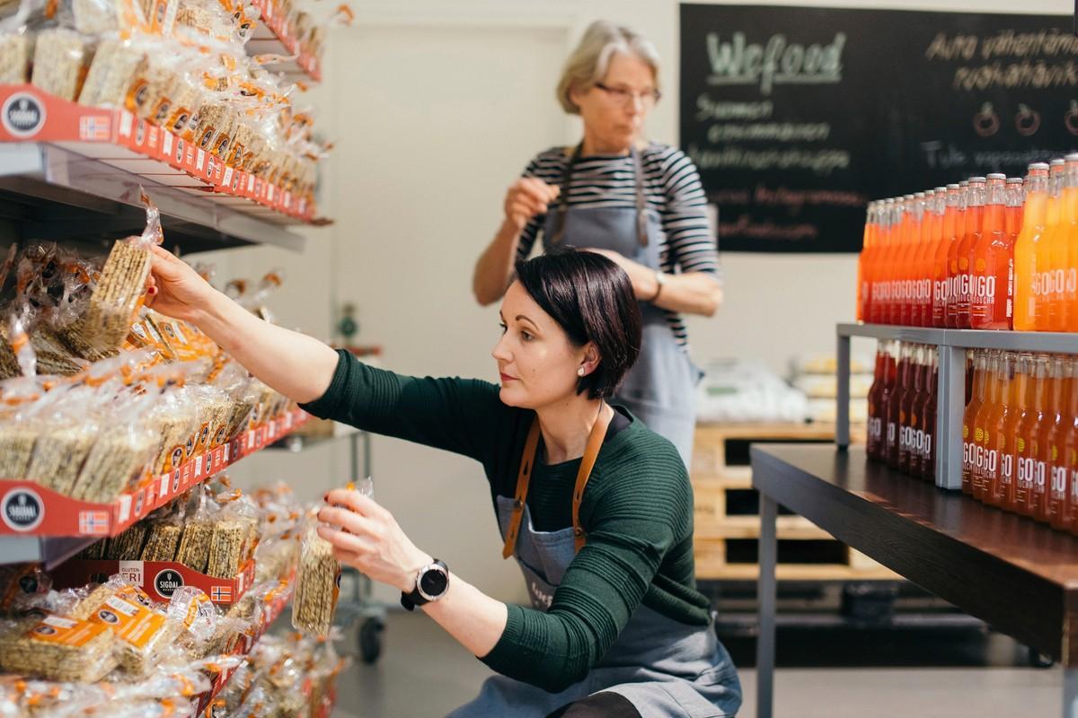 WeFood-myymälän vapaaehtoiset Tanja Mårtensson ja Merja Dahlbom laittavat tuotteita hyllyihin.