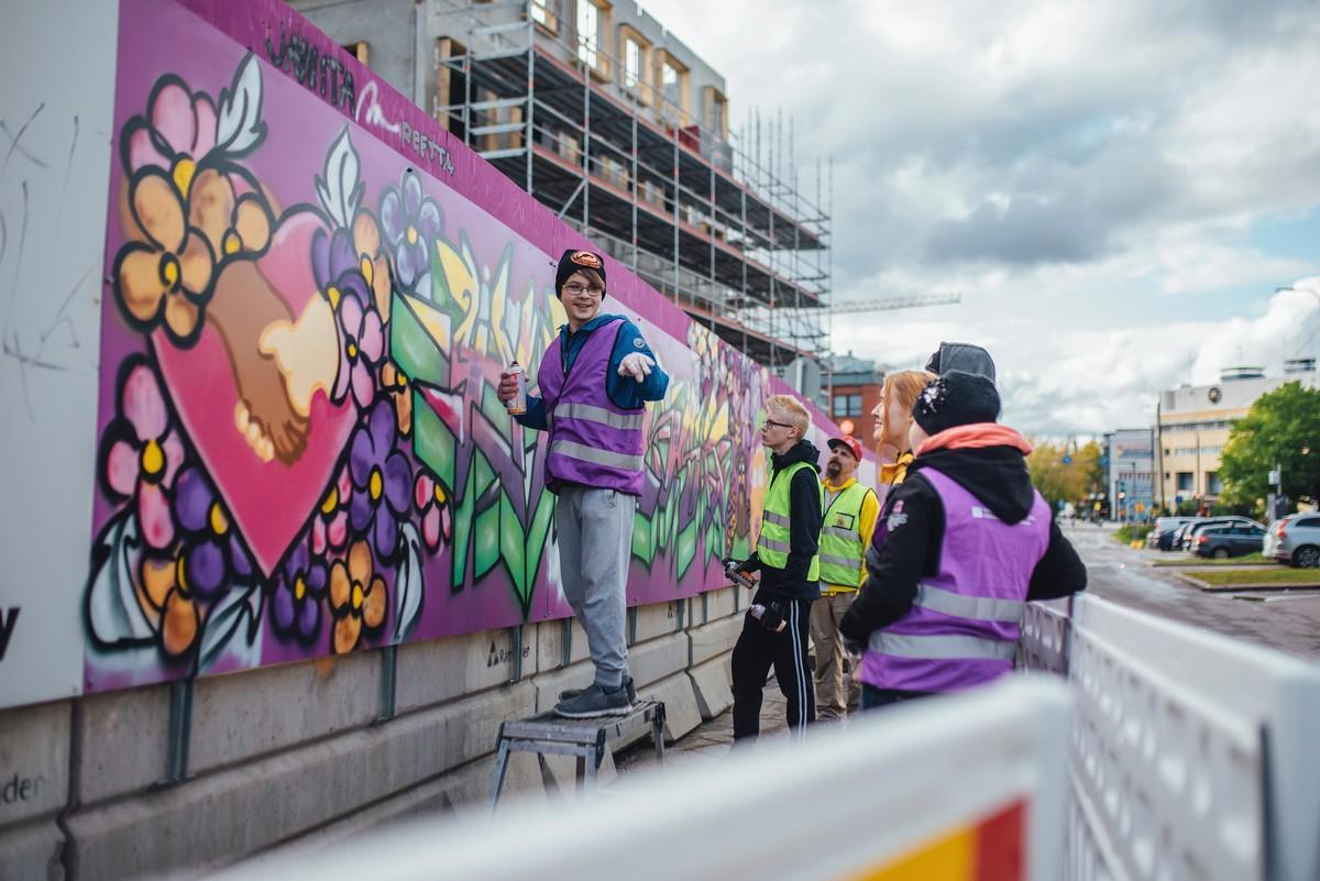 Toivo Pottonen seisoo penkillä maalaamassa osuuttaan Tikkurilan kirkkotyömaan aitaan tehtyyn graffititaideteokseen.