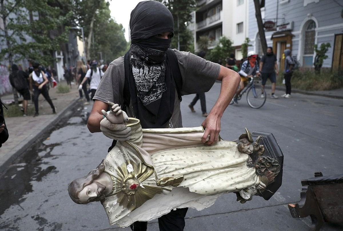 Naamioitu mielenosoittaja kantoi kirkosta ottamaansa Jeesuksen patsasta Santiagossa viime viikon perjantaina.