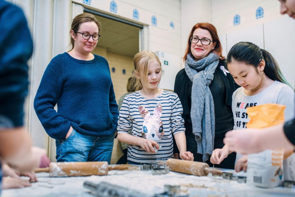 Opettaja Katrianna Raunio ja rehtori Heli Siljama seuraavat, kuinka Emilia Moilanen ja Nina Pham leipovat.