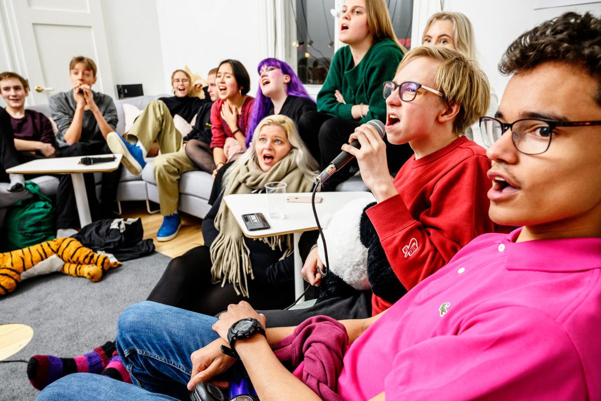 Nuorisopappi Laura Huovinen (lattialla keskellä) laulaa karaokea punapaitaisen Aatos Ehnin ja muiden nuorten kanssa.