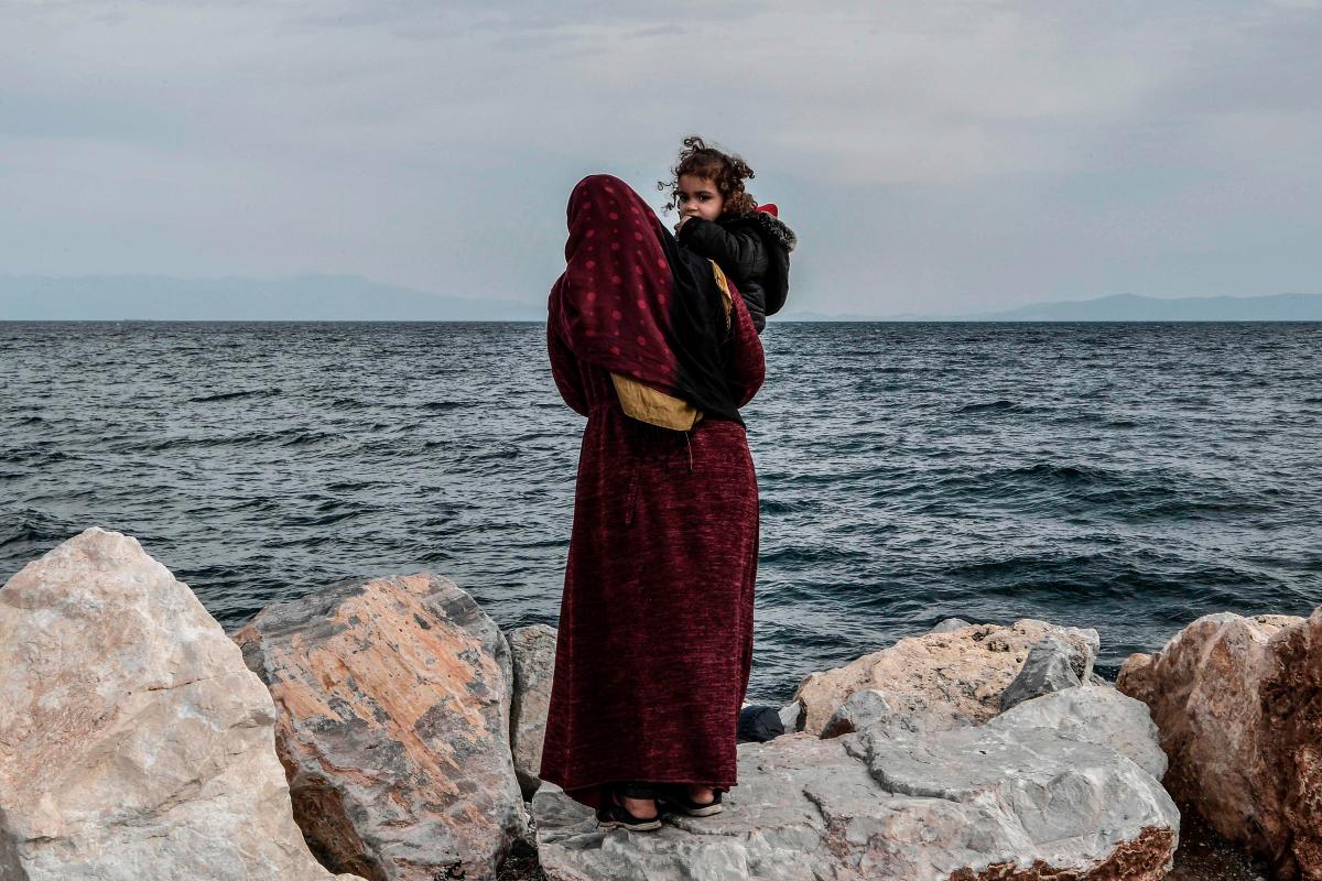 Pakolaisäiti tähyää lapsensa kanssa Kreikan mantereelle päin Mytilenen sataman lähettyviltä Lesboksen saarella 7. maaliskuuta. Louisa Gouliamaki / AFP ─ Lehtikuva