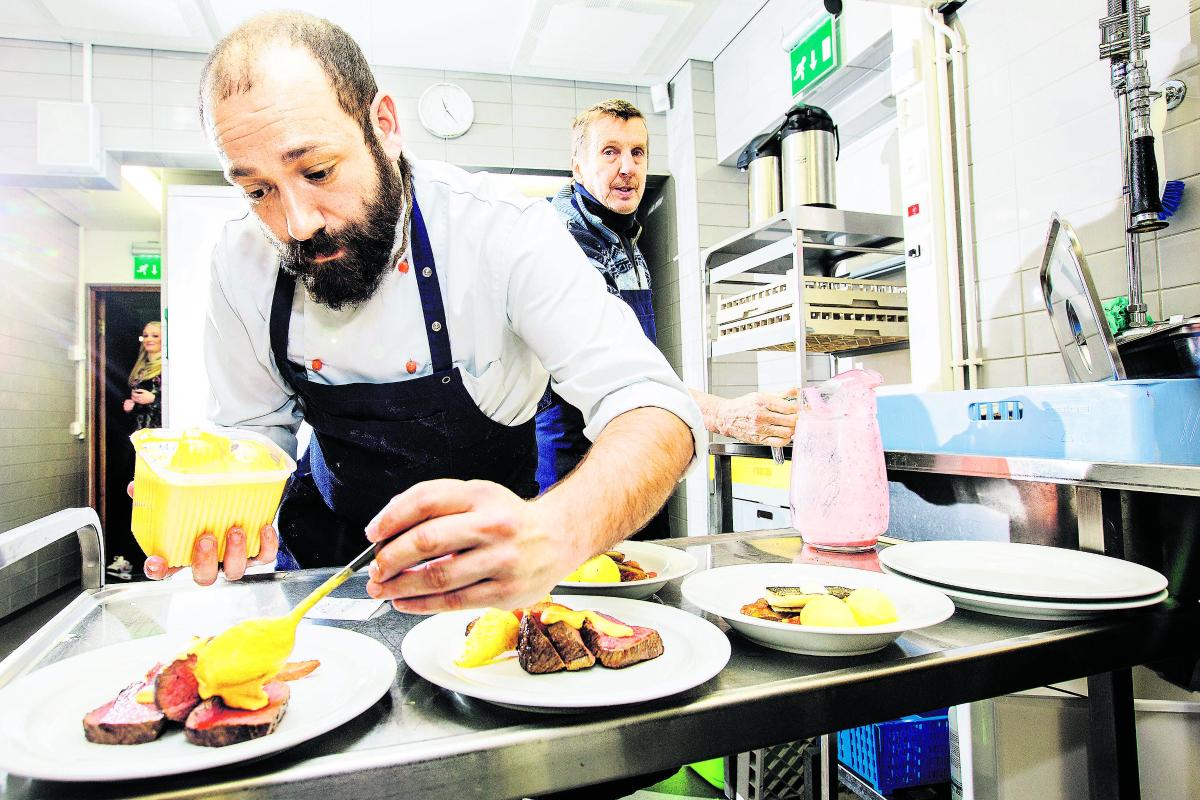 Kuin ravintolassa. Kokki Manuel Alvarez Sanchez viimeistelee pääruokia valuttamalla romesco-kastiketta marmorifileen ja juuresten päälle. Tarjoilija odottaa annoksia takana.