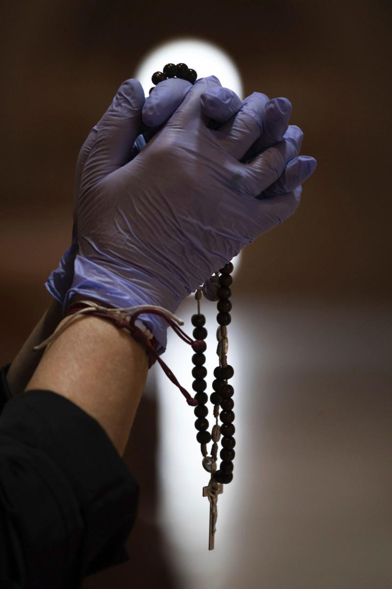Katolilainen rukoilee Espanjassa kädessään suojakäsineet. Espanjassa on nyt voimassa ulkonaliikkumiskielto.