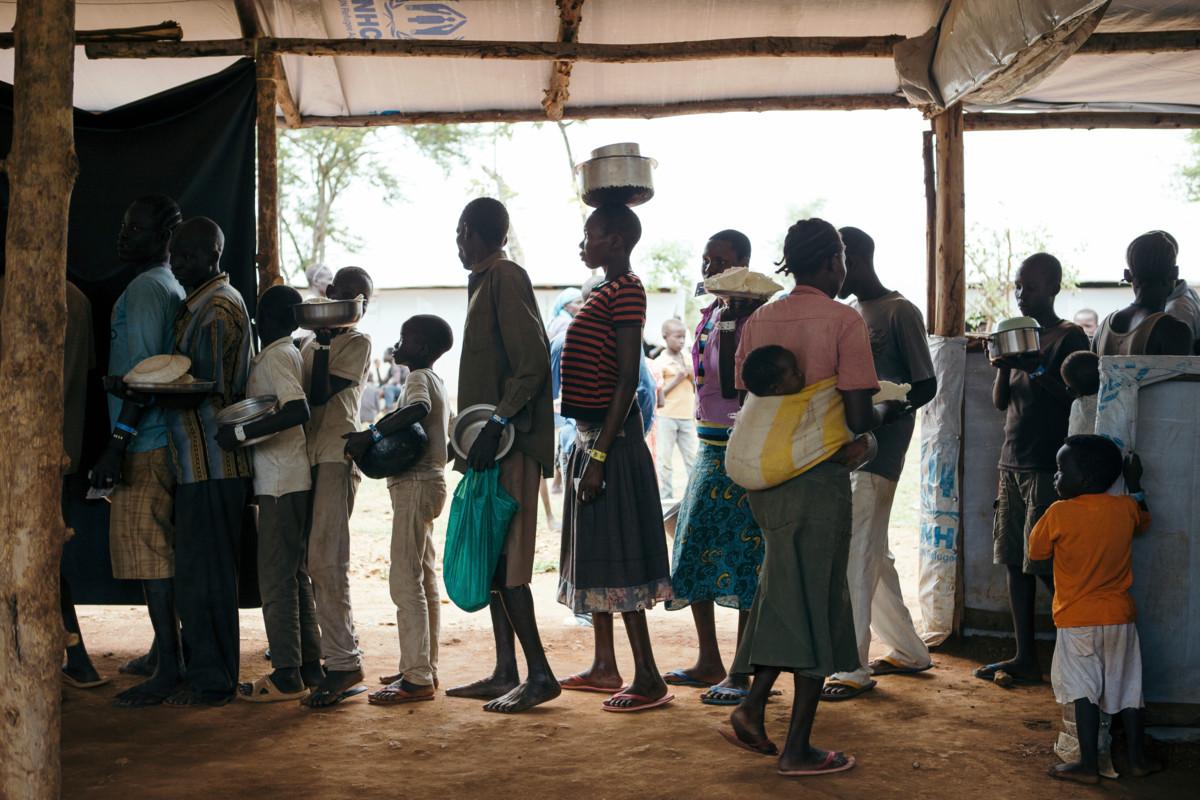 Etelä-Sudanin ja Ugandan välisen rajan ylittäneet ihmiset saapuvat Omugon pakolaisasutusalueen vastaanottokeskukselle. Siellä he viettävät ensimmäisen yönsä ennen kuin heidät sijoitetaan omille alueilleen. Kuvassa jonotetaan ruokaa.