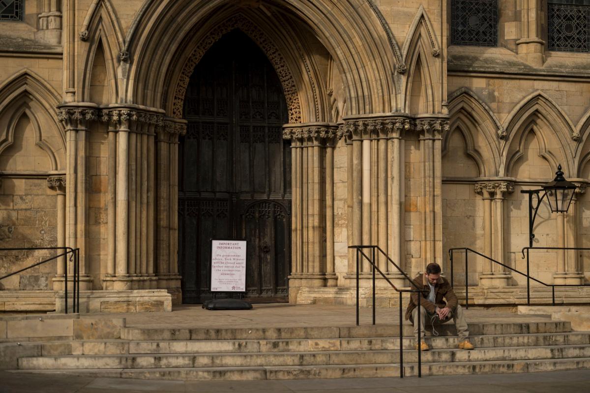 Mies istui Yorkin tuomiokirkon portailla 19. maaliskuuta. Kirkon ovella olevassa ilmoitustaulussa kerrotaan, että kirkko on suljettu koronaviruspandemian vuoksi.