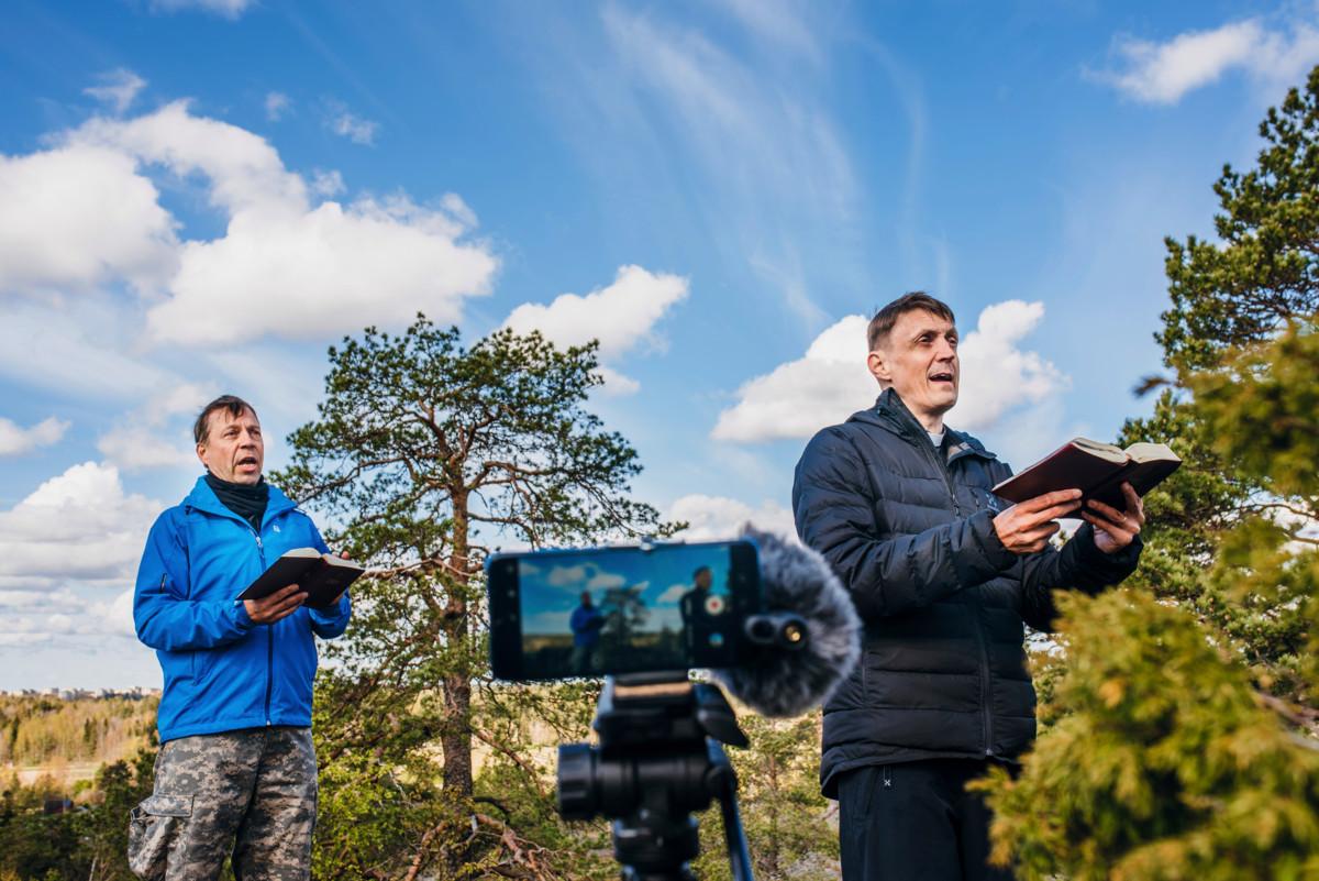 – Högberget on puhutteleva kallio. Voin kuvitella, miten meri on lainehtinut tuhat vuotta sitten alhaalla, missä avautuu nyt peltoaukea, laulaja Hannu Holma sanoo. Oikealla veisaa kirkkoherra Hans Tuominen.