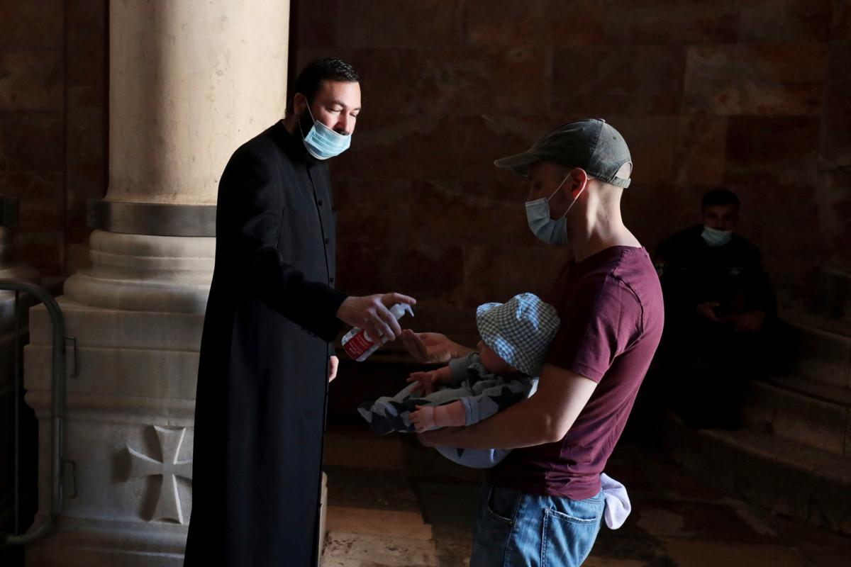 Armenian ortodoksisen kirkon munkki antaa käsidesiä Jerusalemin Pyhän haudan kirkkoon saapuvalle miehelle ja lapselle.