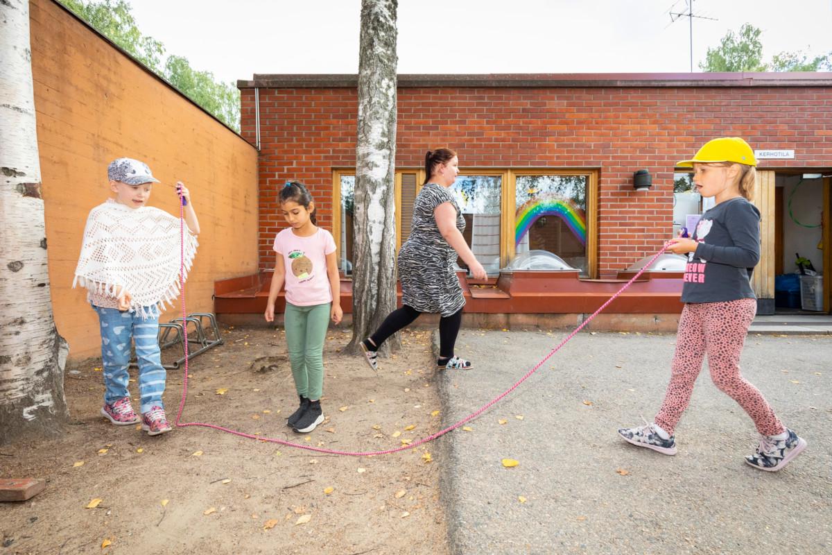 Annabella (vas.), Nathalie ja Isla hyppäävät narua Kivistön kirkon pihalla, taustalla lastenohjaaja Jenny Nikkanen.