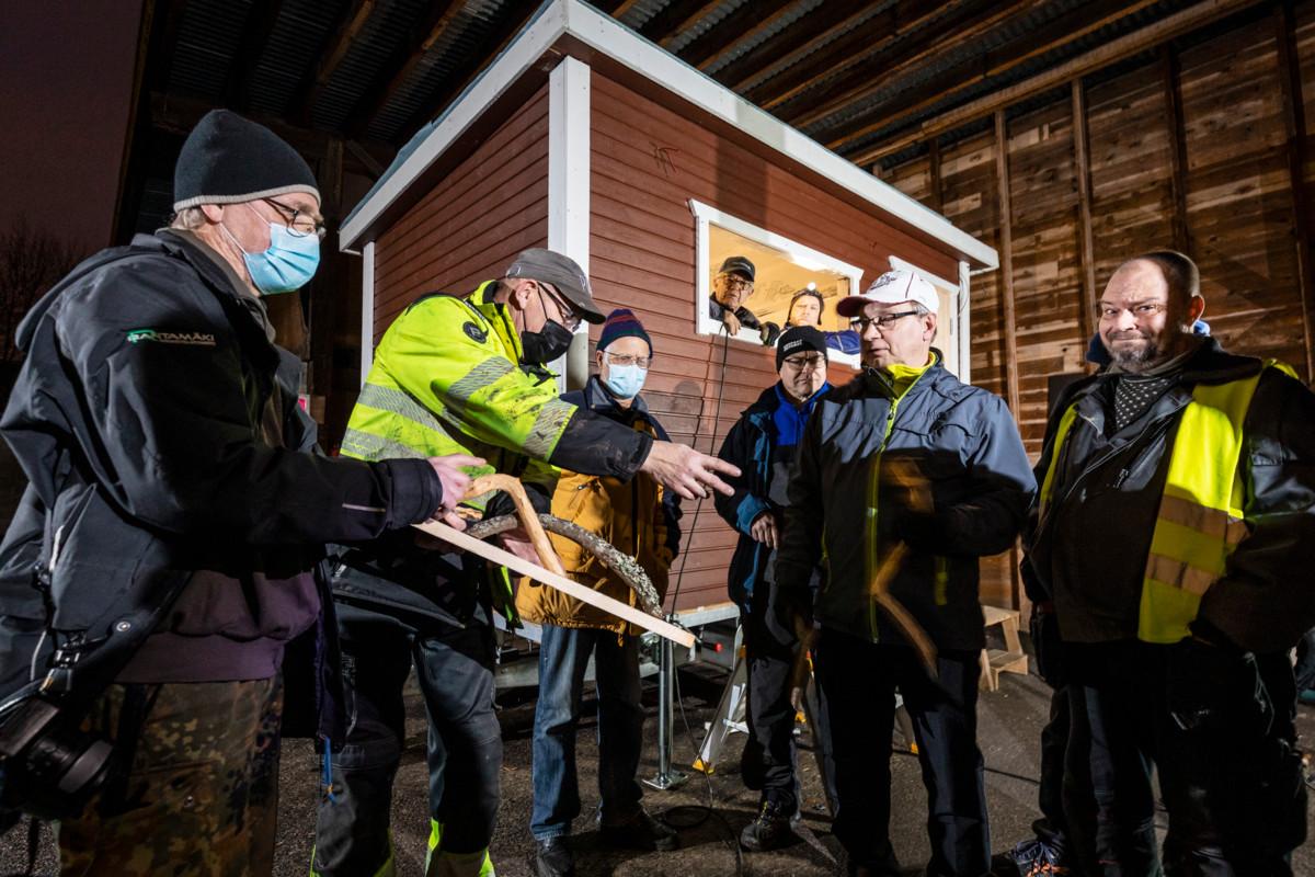 Hannu Andersson (vasemmalla), pappi Jukka Holopainen, Matti Arpiainen, Jussi Rinta-Filppula, Juha Kallio ja Tomppa Virtanen mallailevat saunan ulko-oven kahvavaihtoehtoja. Kauko Mustola ja Esa Järvinen kurkkivat ikkunasta.