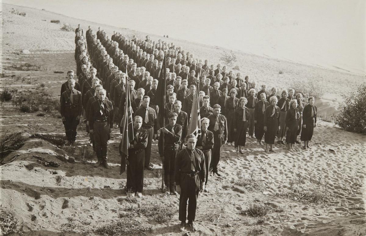 Sinimustien Kuortaneen leiri vuonna 1935. Etualalla pappi Elias Simojoki. Lippujen takana vasemmalta: Paavo Susitaival, Oskari Meriluoto, Viljo Lius ja Reino Ala-Kulju. Äärimmäisenä oikealla lehtori Anna-Liisa Heikinheimo. Simojoki sai toiminnastaan Sinimustissa tuomiokapitulilta muistutuksen sopimattomasta menettelystä papinvirassa.