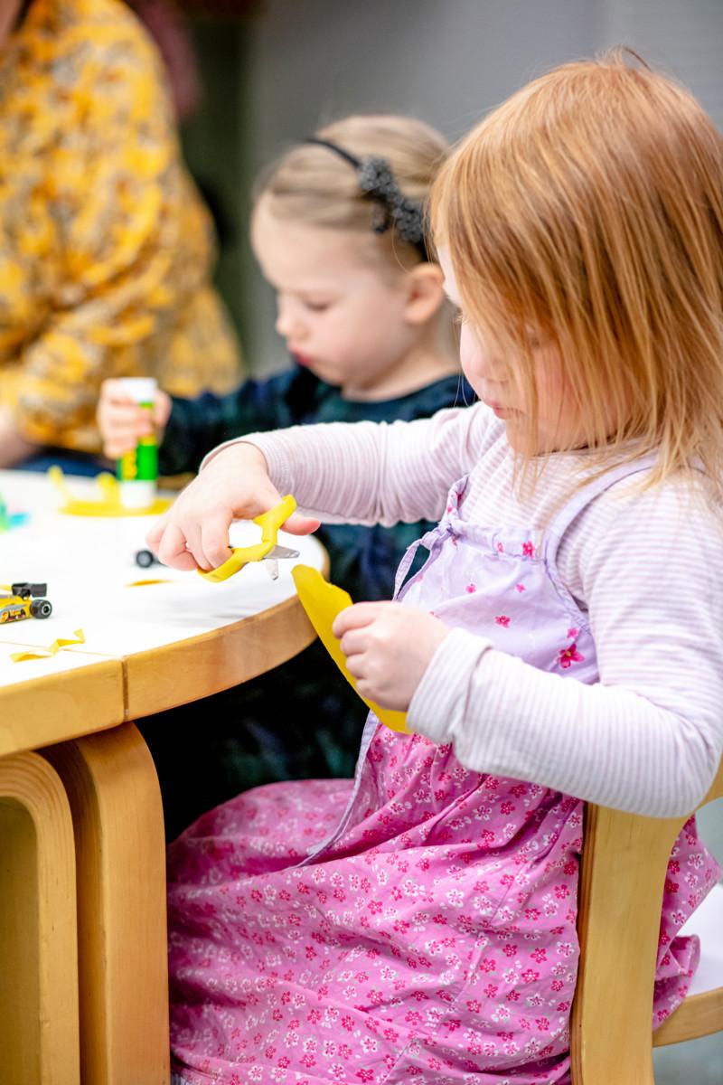 Marni Karumo liimaa höyheniä kartonkiin ja Minttu Leppävuori harjoittelee saksien käyttöä.