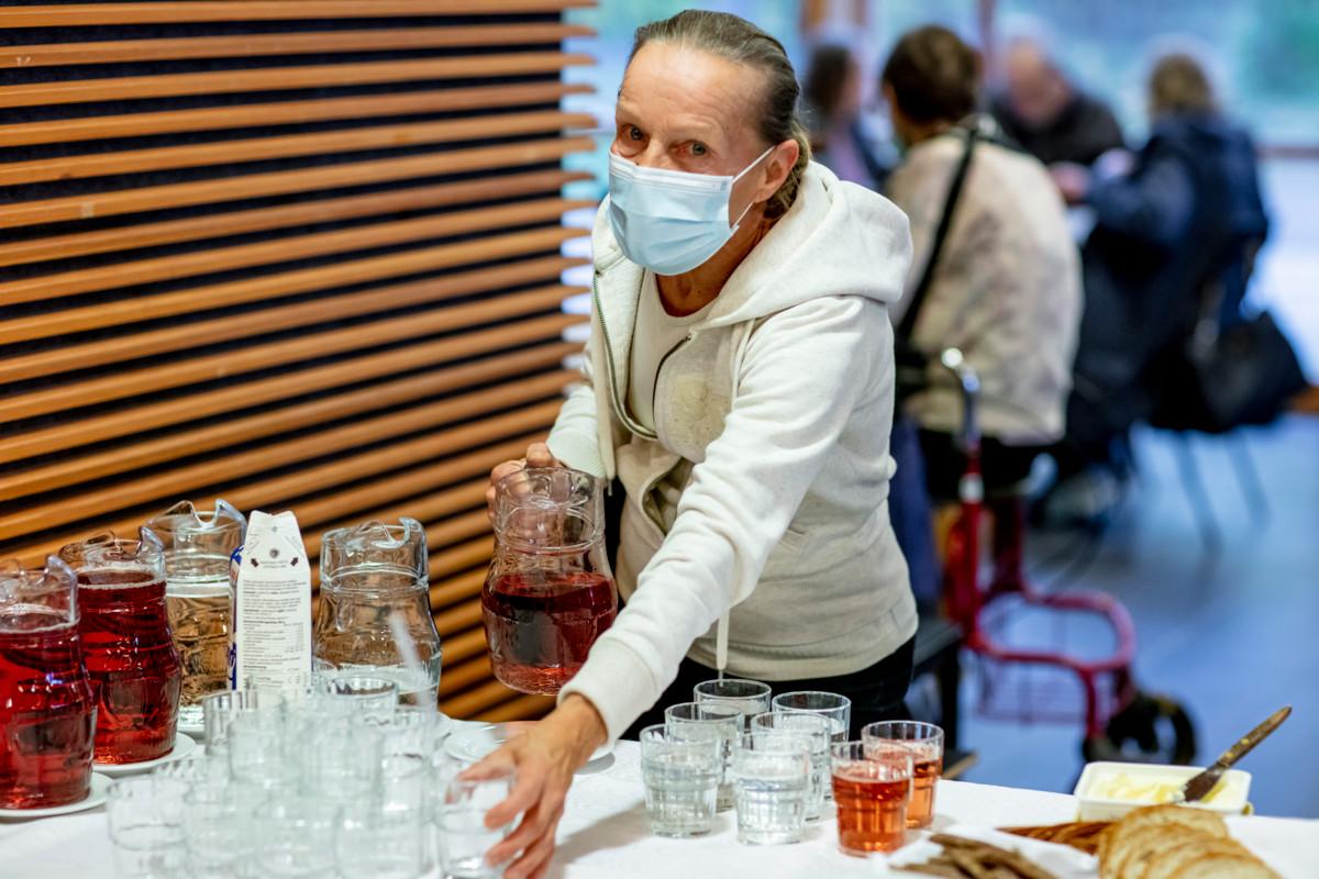 Leena Savolainen jakaa ruokajuomia. Vapaaehtoiset seurakuntalaiset kattavat pöydät, annostelevat ruuan ja kantavat astiat keittiöön.