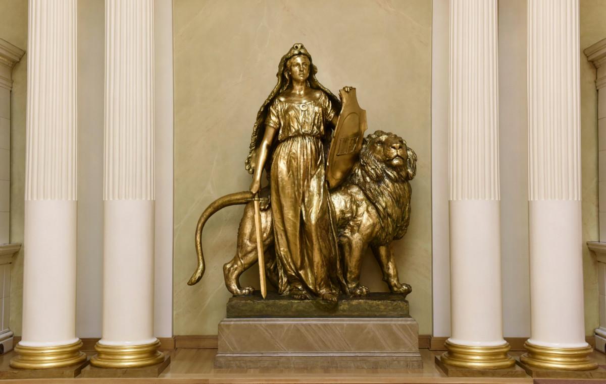 Walter Runebergin Lex-patsaassa karhuntaljaviittainen neito seisoo miekka ja perustuslain kilpi kädessään, vierellään leijona. Patsas valmistui alun perin Senaatintorille Aleksanteri II patsaan kylkeen, mutta siitä on kopio myös presidentinlinnassa (kuvassa) ja säätytalolla.