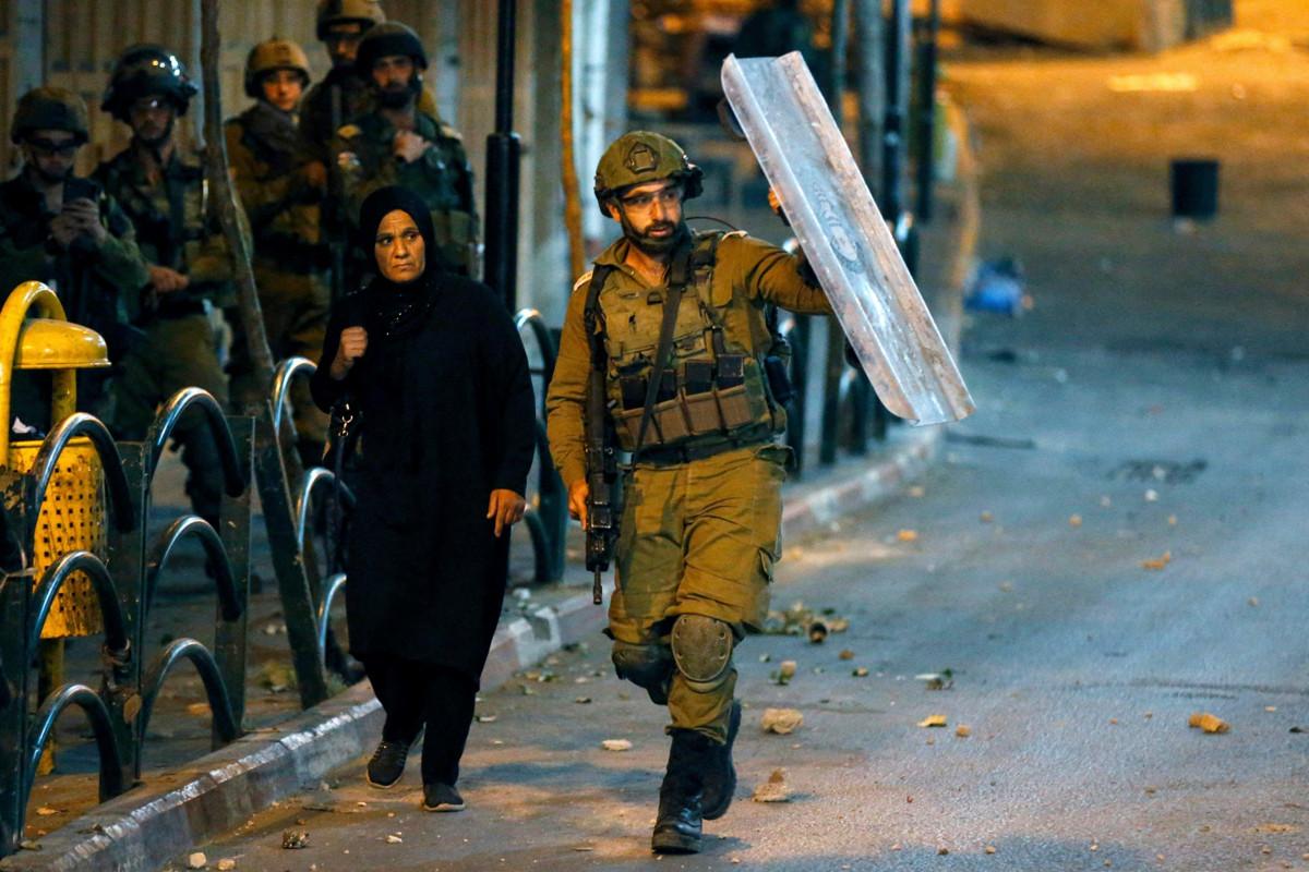Israelilainen sotilas suojasi palestiinalaisnaista Hebronissa Länsirannalla huhtikuussa 2021, kun Israelin turvallisuusjoukot ja palestiinalaiset ottivat yhteen. Kuva: Hazem Bader / AFP photo / Lehtikuva