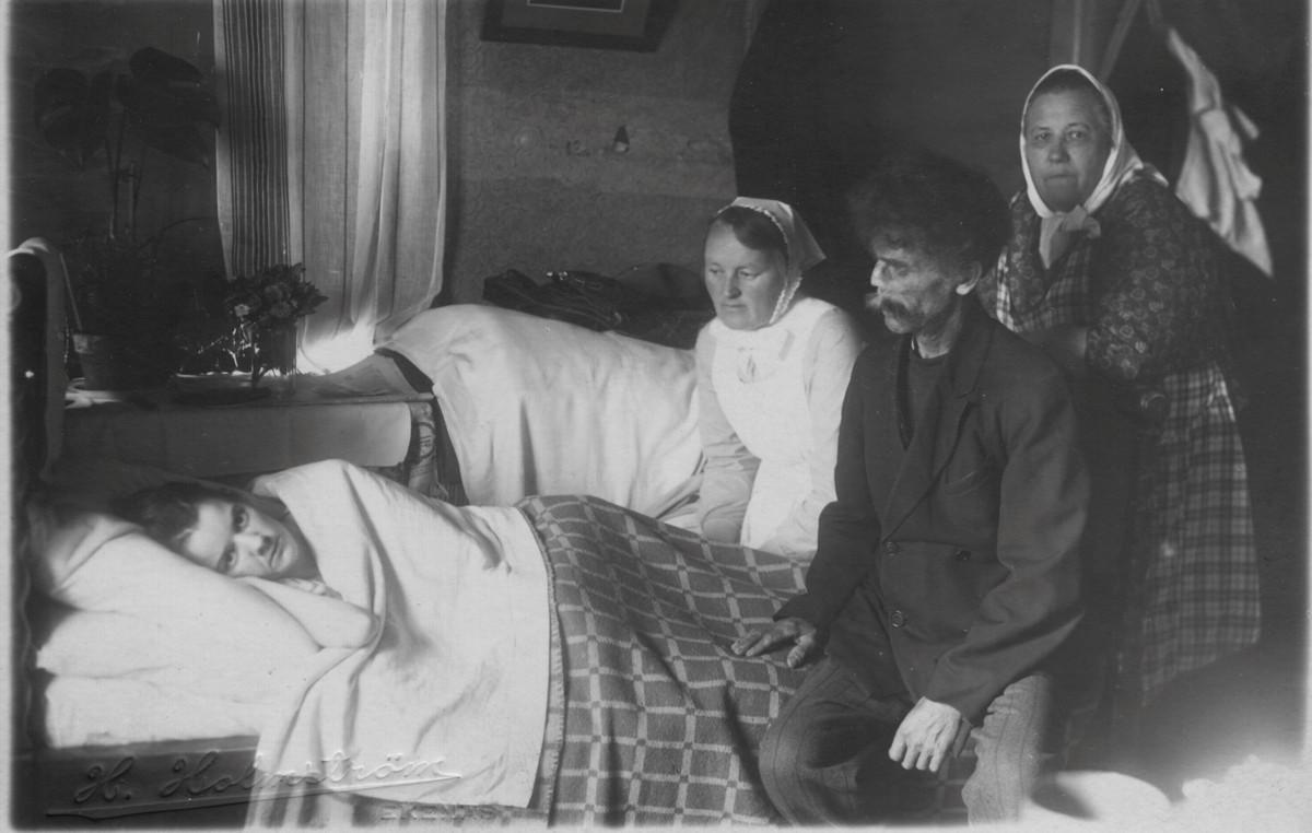 Diakonissa Ester Särs (keskellä) kotikäynnillä potilaan ja hänen omaistensa luona 1920-luvulla. Diakonissan tunnisti puvusta ja päähineestä. Kuva: Diakonissalaitos
