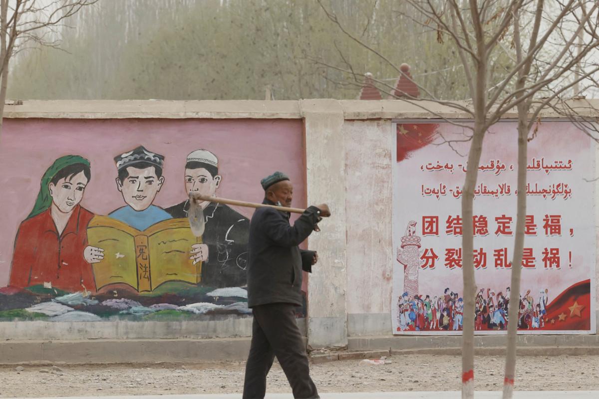 Maanviljelijä kävelee Kiinan hallituksen propagandajulisteen ohi Xinjiangissa. Julisteessa muistutetaan yhtenöisyyden tuovan onnea, separatismin johtavan sekasortoon. Kiina syyttää uiguureja itsenäisyyshaaveista. Kuva: Ng Han Guan/AP/Lehtikuva