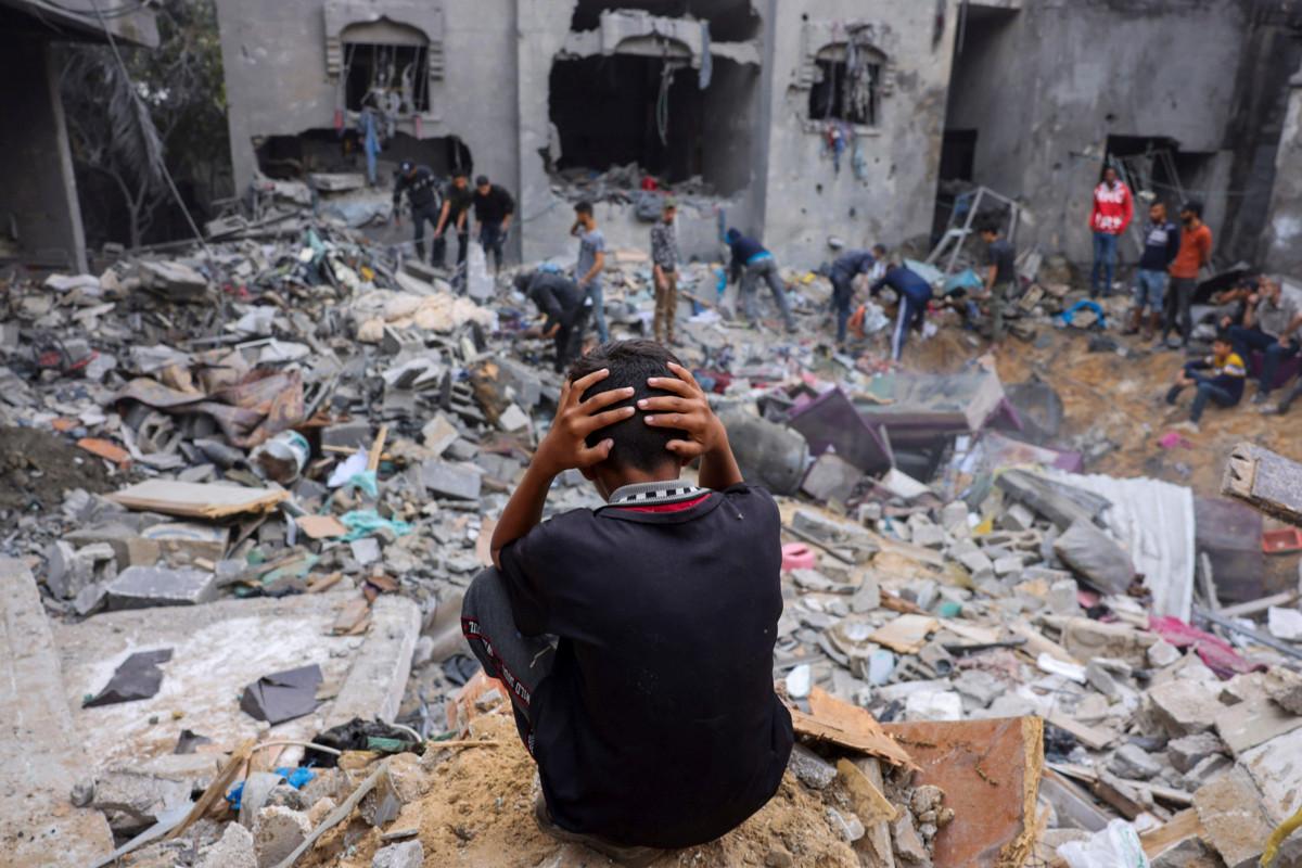 Lapsi seuraa, kun ihmiset yrittävät pelastaa omaisuuttaan tuhotun kerrostalon raunioista Rafahin kaupungissa Gazassa. Kuva: Mohammed Abed/AFP/Lehtikuva
