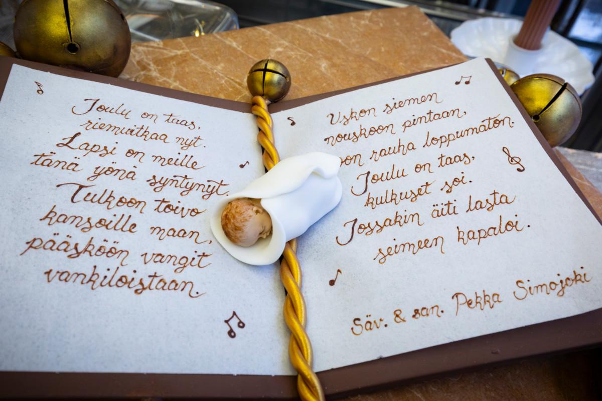 Jeesus-lapsi kellii suklaasta ja sokerista valmistetun kirjan sivuilla, joihin on kirjoitettu suklaalla Tulkoon joulu -laulun sanoja.