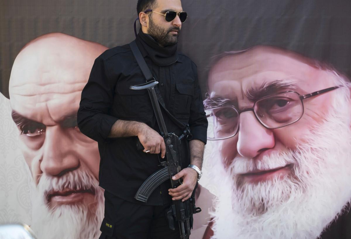 Aseistettu sotilas seisoo vartioimassa julistetta, joka esittää Iranin uskonnollisia johtajia. Vasemmalla on suurajatollahiksi nimitetty islamilaisen tasavallan ensimmäinen johtaja Ruhollah Khomeini, oikealla nykyinen johtaja ajatollah Ali Khamenei. Kuva: Morteza Nikoubazl/NurPhoto/Lehtikuva