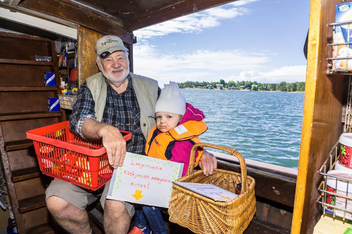 Bill Mikander ja lapsenlapsi Matilda Helmreich keräävät kauppalaivalla lahjoituksia Pirttisaaren kesäjuhlan arpajaisiin. Luvassa on tanssia, musiikkia ja muuta ohjelmaa. Matilda on päässyt juhlan makuun herkuttelemalla suklaajäätelöllä.