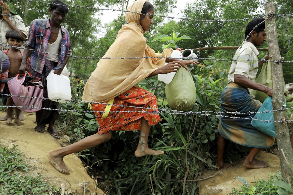 Pakolaiset ylittävät piikkilanka-aidan reunustamaa rajaojaa Myanmarin ja Bangladeshin rajalla.